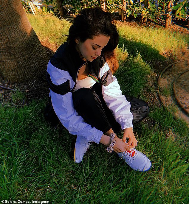 Tying shoes: The 27-year-old singer wore a white top under a black-and-white jacket and matching sweatpants along with purple Puma shoes with a red tongue and white laces